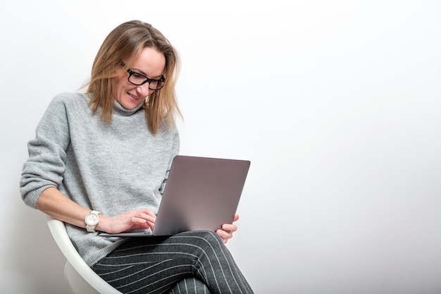 Blond woman with glasses working on computer telecommuting concept isolated on gray