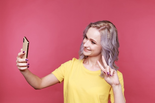 Blond young stylish woman with curly hair showing peace and making photo isolated in the studio