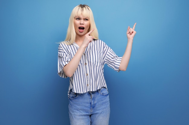 Blond young woman in shirt in showing thumbs up on studio background with copy space