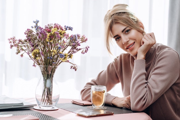 Blonde aantrekkelijke vrouw zit aan de tafel in een café met een dop thee