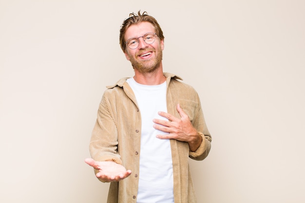 Blonde adult caucasian man feeling happy and in love, smiling with one hand next to heart and the other stretched up front