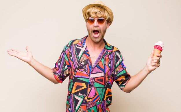 Blonde adult man holding an ice cream with a hat and sun glasses