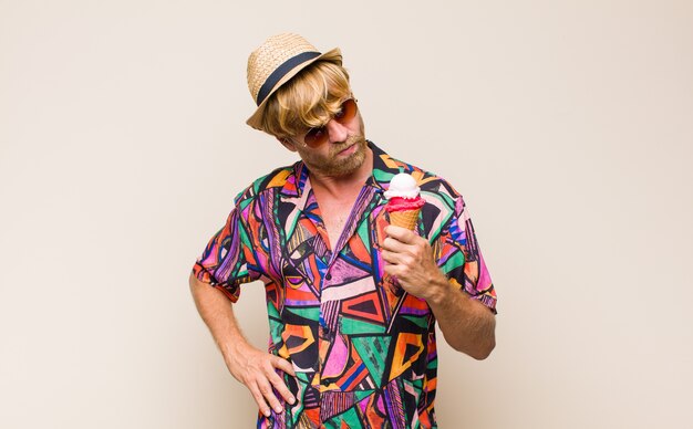 Blonde adult man holding an ice cream with a hat and sun glasses