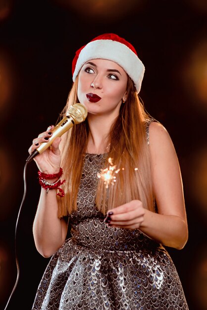 blonde attractive woman in red sweater and red santa hat with microphone and sparkler on stage