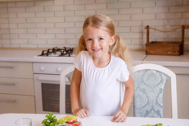 Blonde baby girl eating vegetables in the kitchen