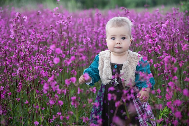 blonde baby in een gekleurde jurk die in een veld met paarse bloemen staat