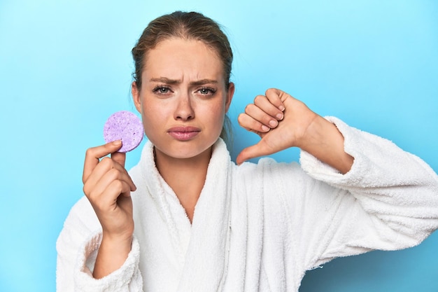 Blonde in bathrobe with facial sponge in studio feels proud and self confident example to follow