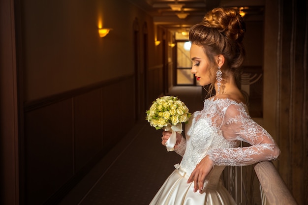 Blonde beautiful bride in fashionable wedding dress with bouquet of roses in hands