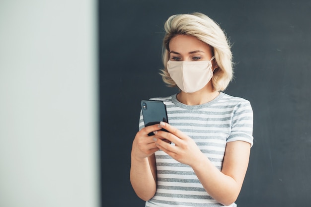 Blonde blanke dame met masker thuis chatten op mobiel