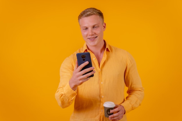 Blonde blanke man op een gele achtergrond die met de telefoon werkt