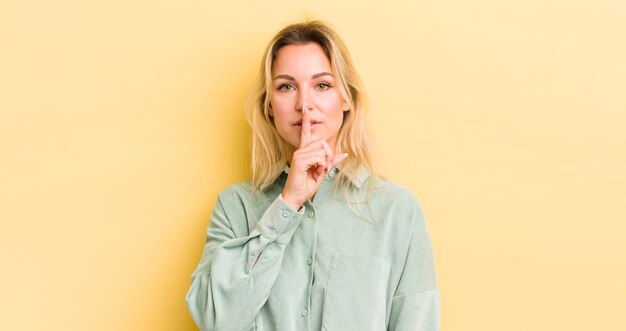 Foto blonde blanke vrouw die er serieus uitziet en kruist met de vinger tegen de lippen gedrukt en eist stilte of stilte om een geheim te bewaren