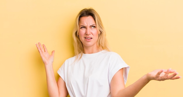 Blonde blanke vrouw die haar schouders ophaalt met een domme, gekke verwarde, verbaasde uitdrukking die zich geïrriteerd en geen idee voelt