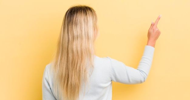 Blonde blanke vrouw die staat en wijst naar een object op het achteraanzicht van de kopieerruimte