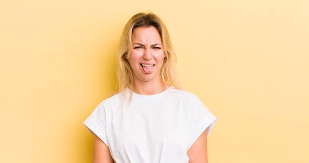 Blonde blanke vrouw die walgt en geïrriteerd voelt, tong uitsteekt en een hekel heeft aan iets smerigs en vies