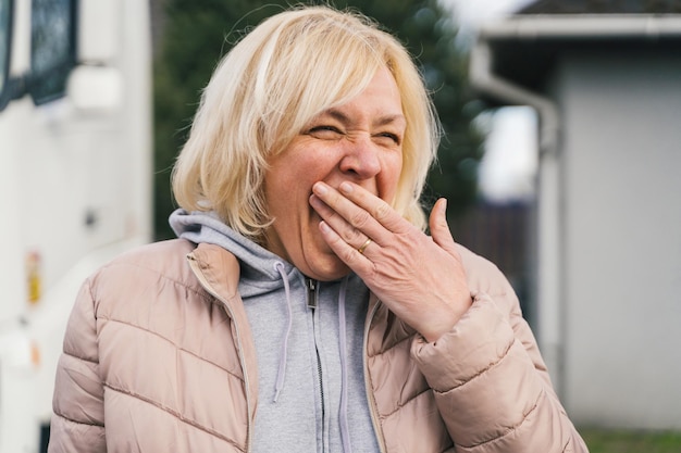 Blonde blanke vrouw van middelbare leeftijd gaapt buitenshuis