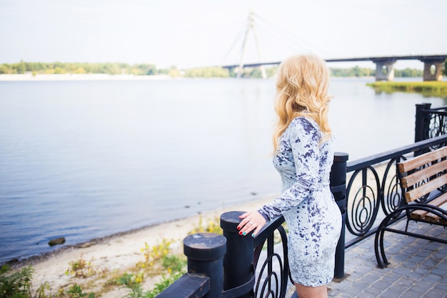 都市公園の川の近くでポーズをとって青いドレスを着た金髪