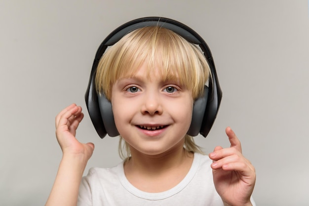 Blonde boy in headphones on light background Child listens to music and smiles