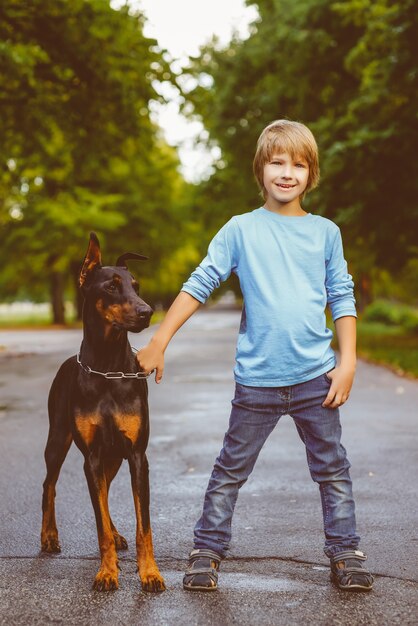 Ragazzo biondo abbraccia con dobermann nel parco estivo