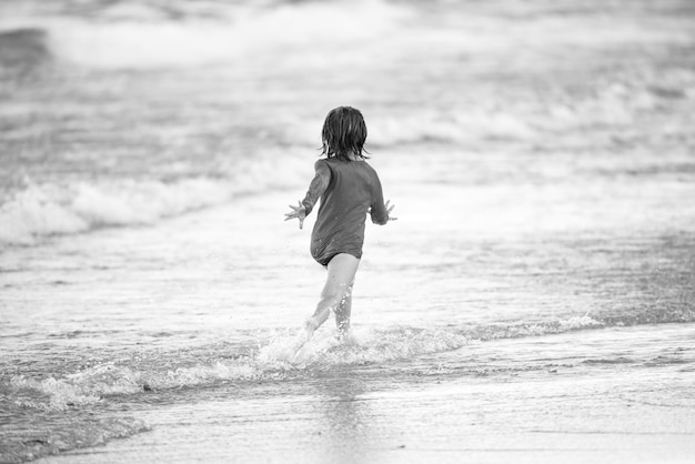 Blonde boy running and having fun on the beach on blue sea in summer