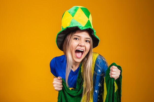 Blonde braziliaanse fan viert op gele achtergrond met braziliaanse vlag