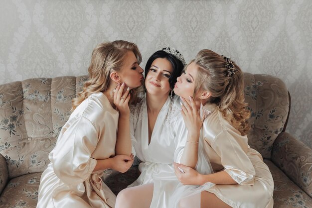 A blonde bride is sitting in a wooden chair wearing a robe and a long veil wedding portrait wedding photo in a light key Beautiful makeup and hair Morning of the bride