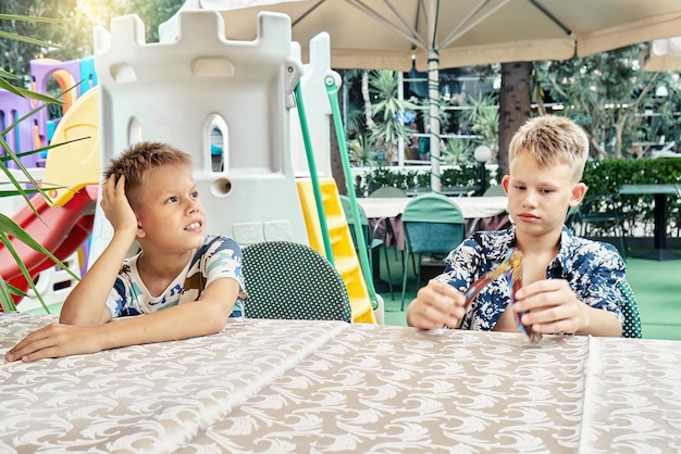 Blonde broers zitten aan de restauranttafel en spelen terwijl ze wachten op de lunch