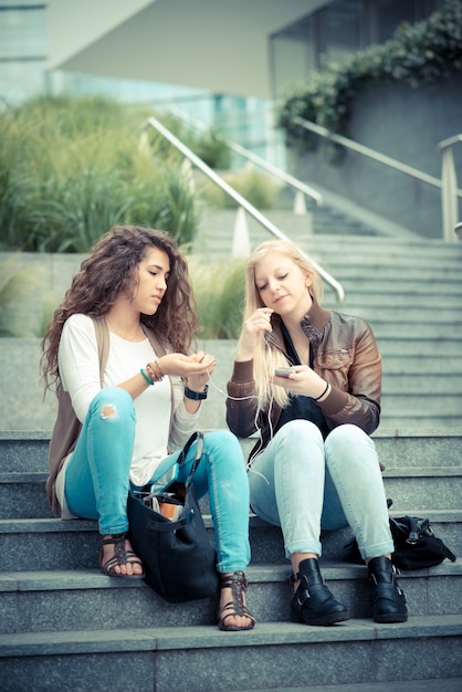 Photo blonde and brunette beautiful stylish young women using smart phone