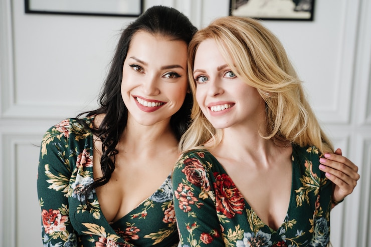Photo blonde and brunette in short green dresses with patterns. two beautiful girls in a white studio.