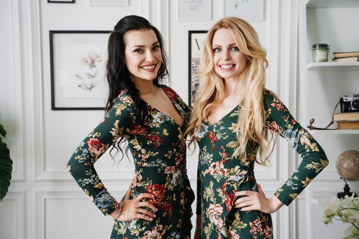 Photo blonde and brunette in short green dresses with patterns. two beautiful girls in a white studio.