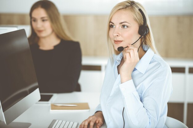 Blonde business woman sitting and communicated by headset in call center office Concept of telesales business