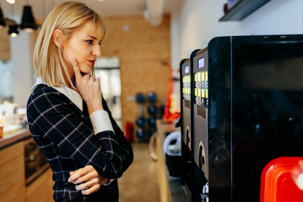 Blonde businesswoman standing in front of a coffee maker in an office cafeteria