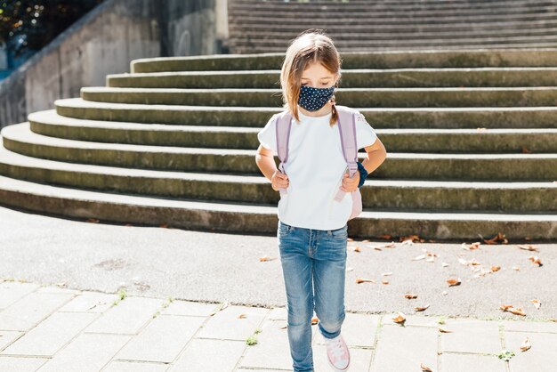 Blonde caucasian girl going to school at the beginning of the year with a mask on her face because of the covid19 coronavirus pandemic