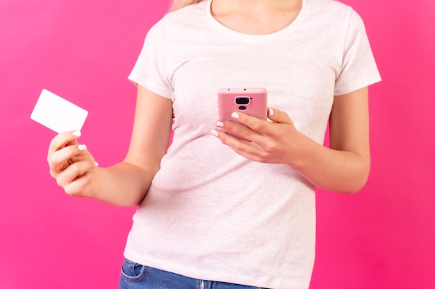 Blonde caucasian girl in pink studio background copy space making a payment with a credit card