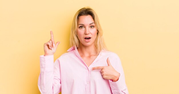 Blonde caucasian woman feeling proud and surprised pointing to self confidently feeling like successful number one