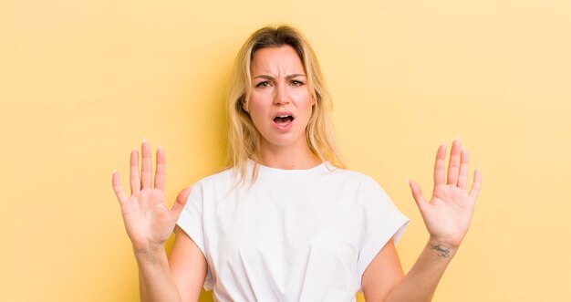 Blonde caucasian woman feeling stupefied and scared fearing something frightening with hands open up front saying stay away