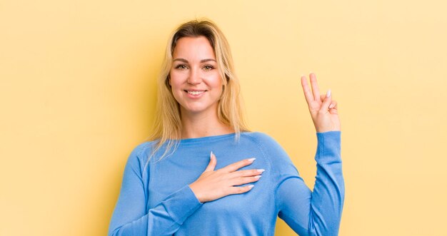 Blonde caucasian woman looking happy confident and trustworthy smiling and showing victory sign with a positive attitude