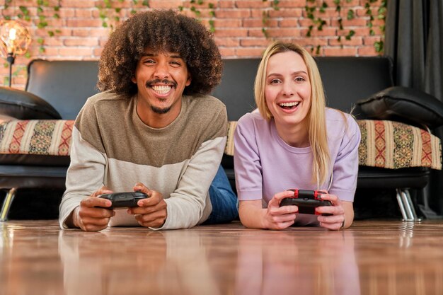 Blonde caucasian young girl and african american young boy lying on the floor playing video game