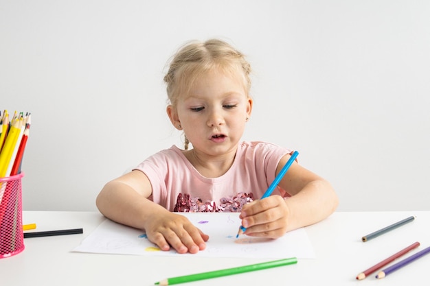 金髪の子供の女の子がテーブルに座って色鉛筆で描く