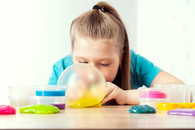 A blonde child inflates a bottle of yellow slime