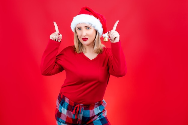 Blonde in Christmas pajamas on a red background shows gestures with her index fingers