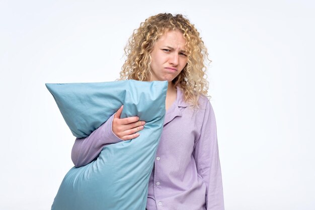 Blonde curly woman holding blue pillow feeling sleepy