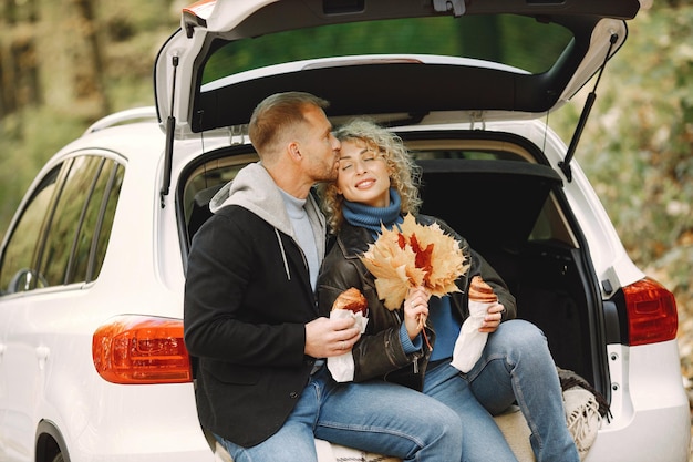 Blonde curly woman and man sitting in a trunk in car in autumn forest and hugging