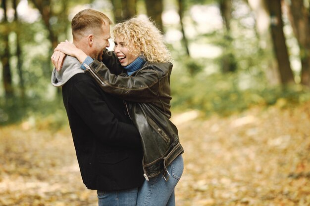 Blonde curly woman and man standing in autumn forest and hugging