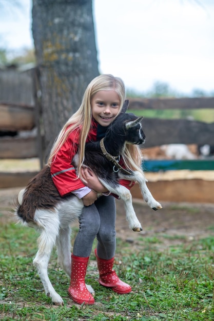 A blonde cute girl playing with a goat on farm