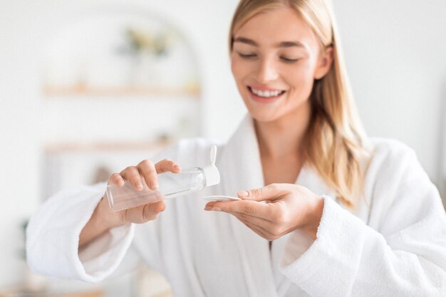 Blonde dame met katoenen pad en micellar water in de badkamer