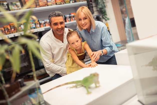 Blonde daughter feeling excited while looking at iguana with parents