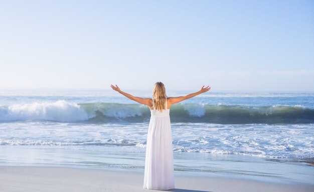 Blonde die zich bij het strand in witte sundress met uit wapens bevinden