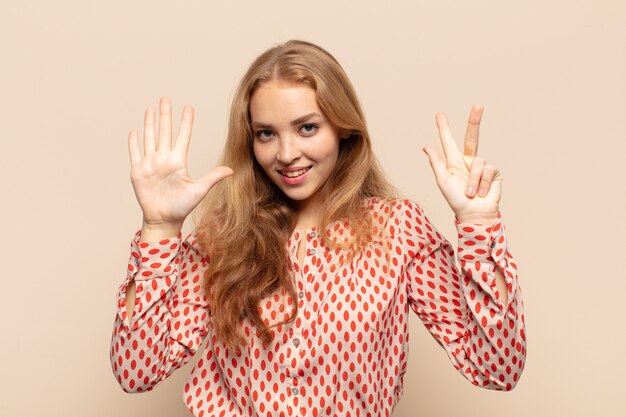 Blonde en vrouw die vriendelijk glimlacht kijkt, nummer acht of achtste met vooruit hand toont, aftellend