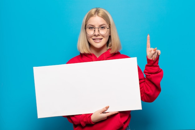 Foto blonde en vrouw die vriendelijk glimlacht kijkt, nummer één toont of eerst met vooruit hand, aftellend