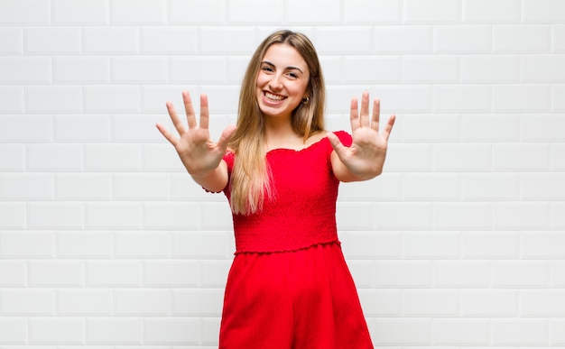 Blonde en vrouw die vriendelijk glimlacht kijkt, nummer tien of tiende met vooruit hand toont, aftellend